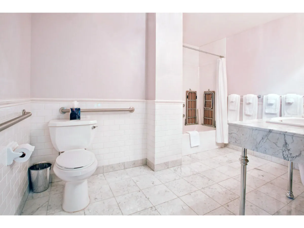 A serene and modern bathroom space featuring a marble sink, a toilet with grab bars, a bathtub with a towel, and plush towels displayed nearby. The overall design exudes calm, with soft lighting and clean lines, inviting a sense of comfort and relaxation.