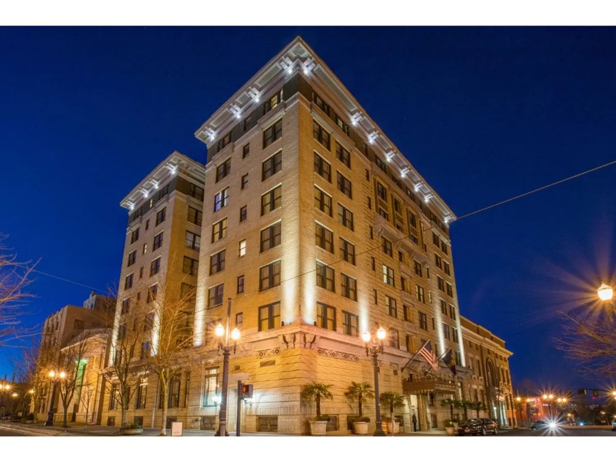 An ornate building facade illuminated at dusk, with street lamps casting a warm glow and inviting the eye toward the surrounding vibrant cityscape. The scene hints at nearby attractions and the walkable, lively environment guests can enjoy.